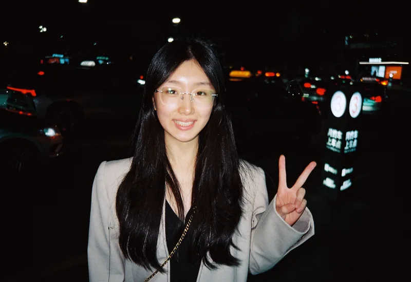 抵达当晚，她戴着眼镜在车辆旁对镜头微笑比耶