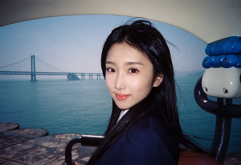 她在海边回头看镜头，远处有跨海大桥