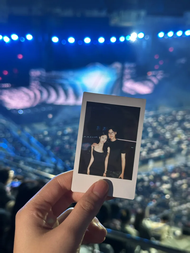手持双人拍立得合照，背景是演唱会蓝色舞台灯光