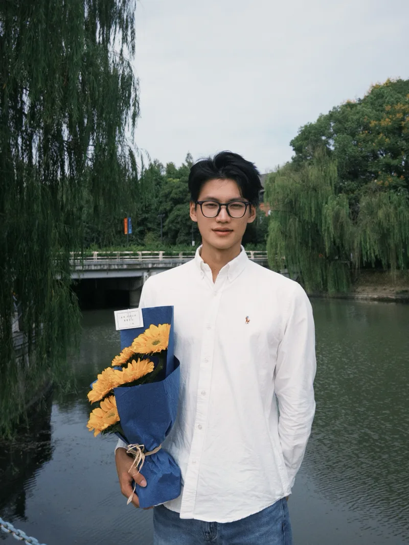 浙大面试结束后，他穿着白衬衫抱着蓝色包装的黄色花束，站在校园水边
