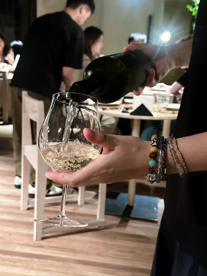 餐馆里，一只手托着高脚杯，另一只手从酒瓶中倒入酒液