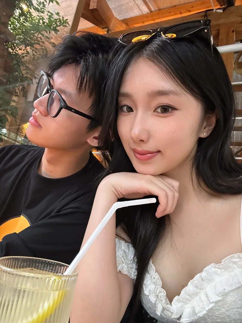 她托着下巴看向镜头，他坐在旁边，前景有带吸管的饮品