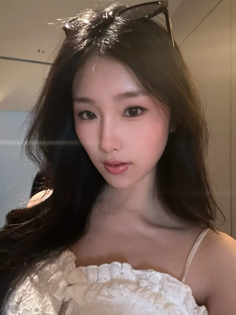 她穿白色上衣，头上架着墨镜，看向镜头的近照