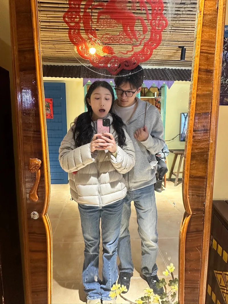 两人在木框全身镜前自拍，她挽着他的手臂