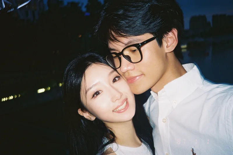 她靠在他身旁对镜头微笑，他低头看向她