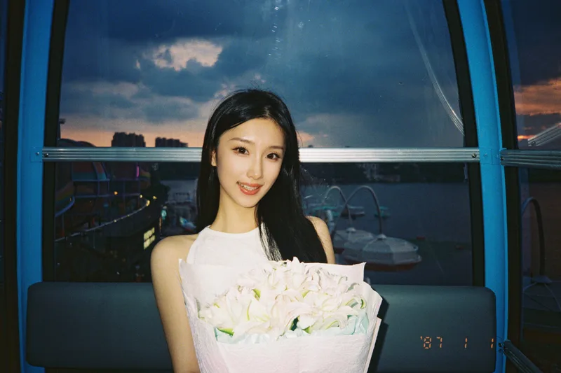 她在蓝色窗框前抱着花束，窗外是湖面和傍晚的天空