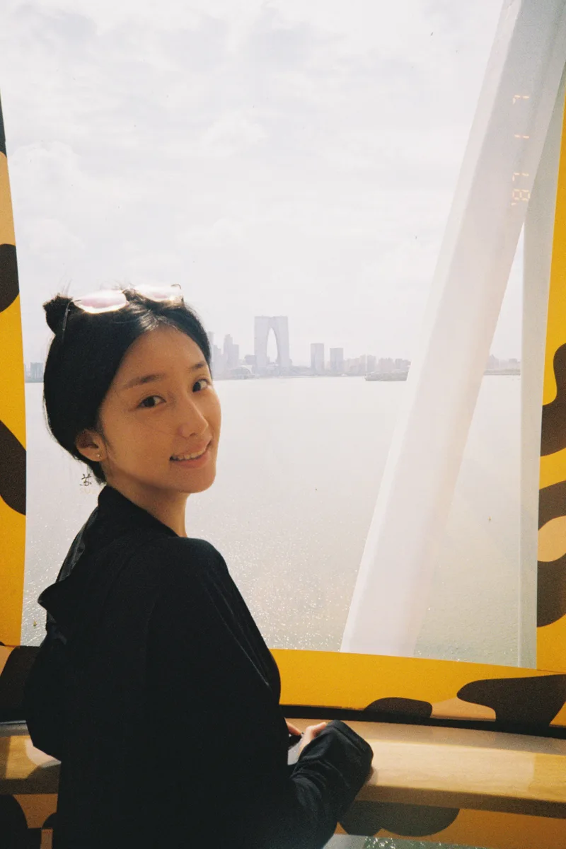 她站在同一轿厢的窗边，回头对镜头微笑，窗外是金鸡湖